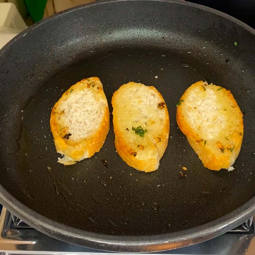 unas rebandas de pan tostándose en una sartén con aceite de oliva ajo y perejil