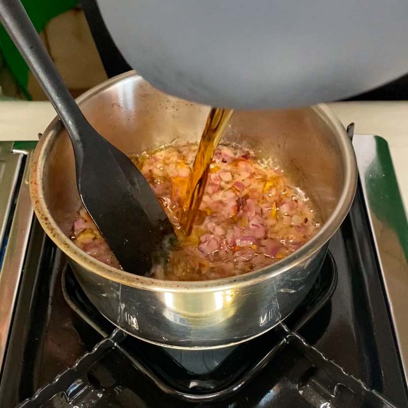 cebolla morada pochándose en mantequilla mientras se le añade brandy para hacer una salsa de boletus