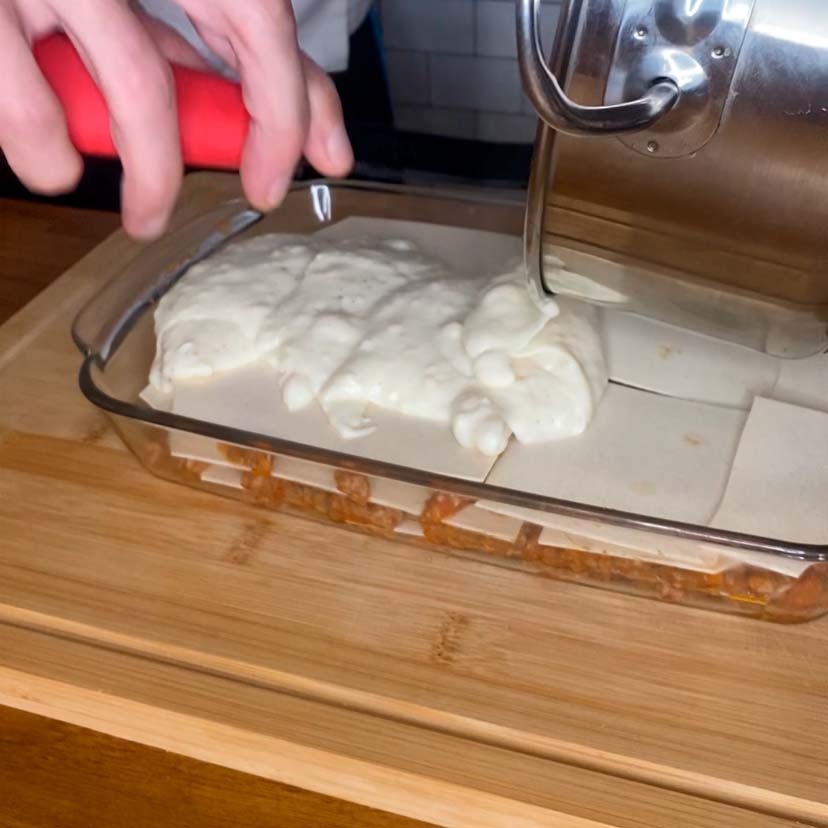 una bandeja con una lasaña montándose con una capa de bechamel