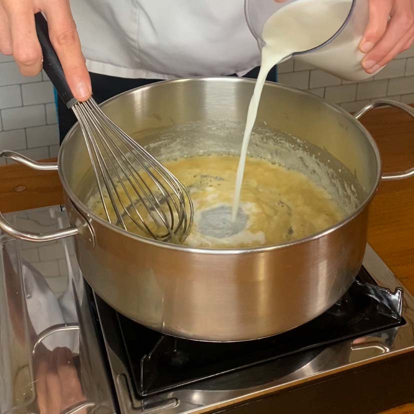 Una olla con un roux, mientras se le añade leche poco a poco para hacer una receta salsa bechamel casera